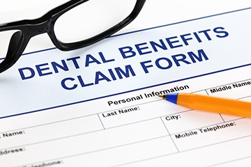 Top of a blue dental benefits claim form with black rimmed glasses