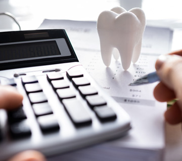 Person typing on a calculator next to a model of a tooth