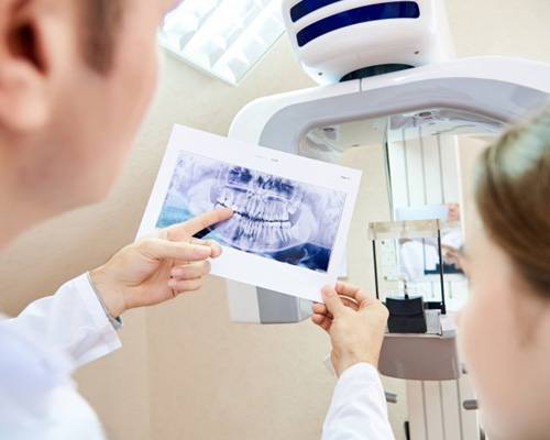 Dentist pointing to a patient’s X-ray next to CBCT scanner